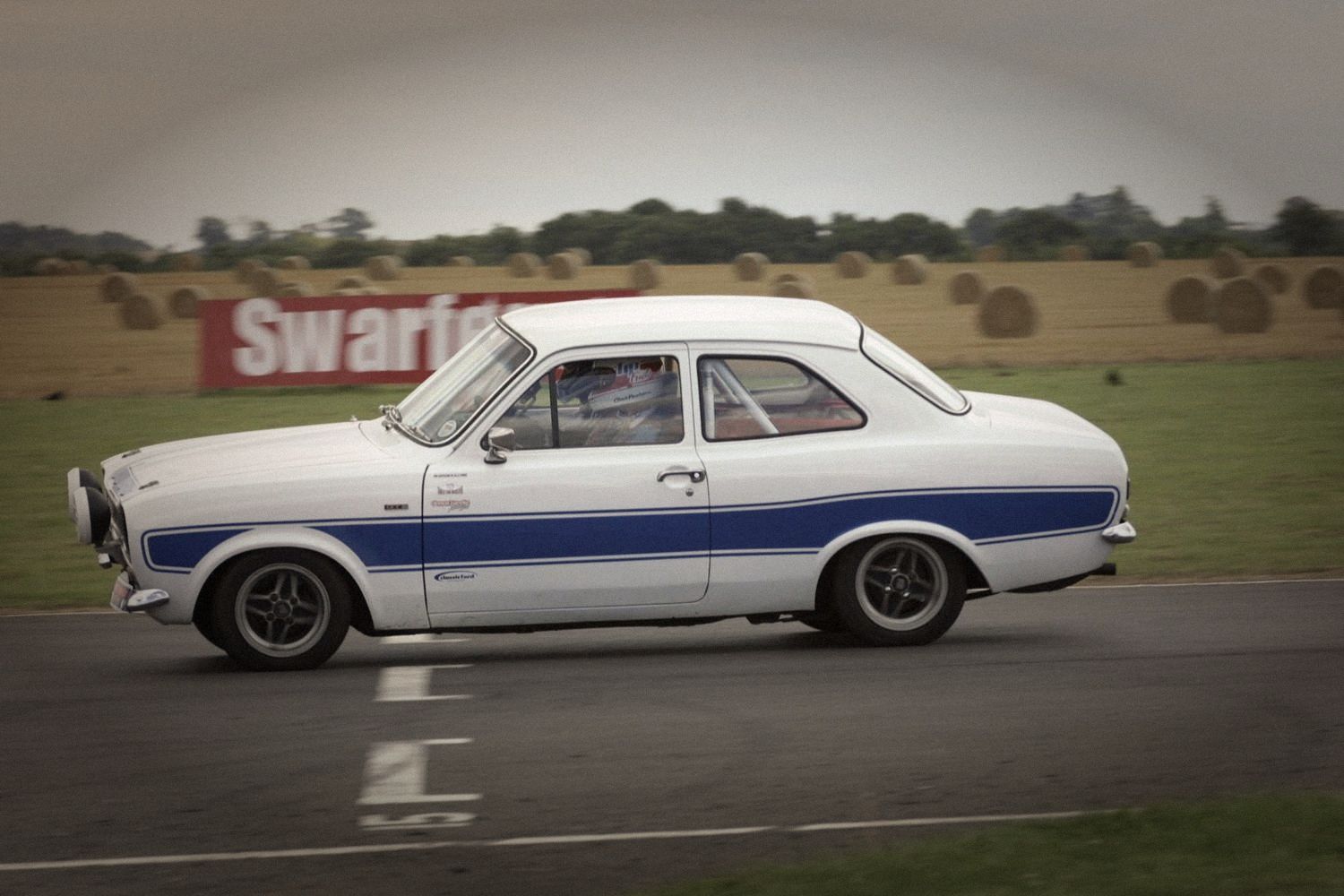A white Mk1 Ford Escort with blue stripes on track